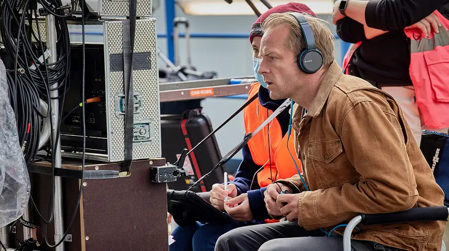Regisseur Hinnerk Schönemann beim Dreh von „Blindgänger“ blickt auf einen Monitor und hat Kopfhörer auf.
