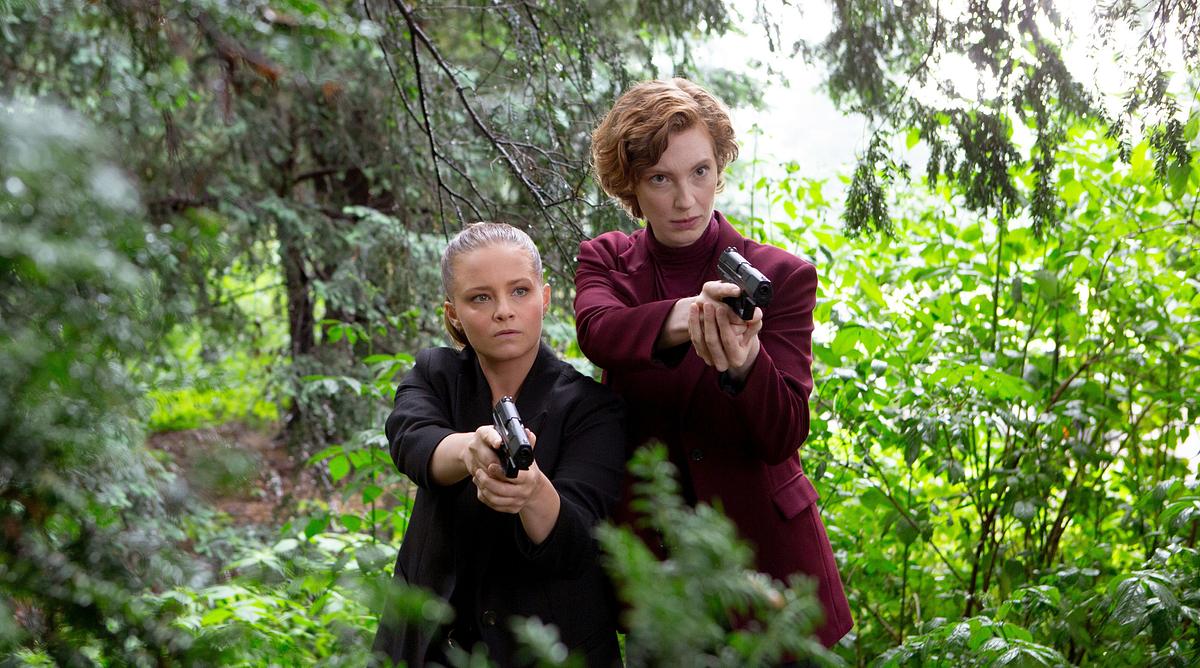Tatort Angst im Dunkeln Jasna Fritzi Bauer und Luise Wolfram stehen in einem Wald und zielen mit ihren Schusswaffen. Bauer trägt schwarz und Wolfram rot.