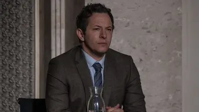 Dr. Martin Roth sitzt mit konzentriertem Blick an einem Tisch. Er hat die Hände gefaltet und einen Anzug an. - Foto: © Prime Video, Britta Krehl