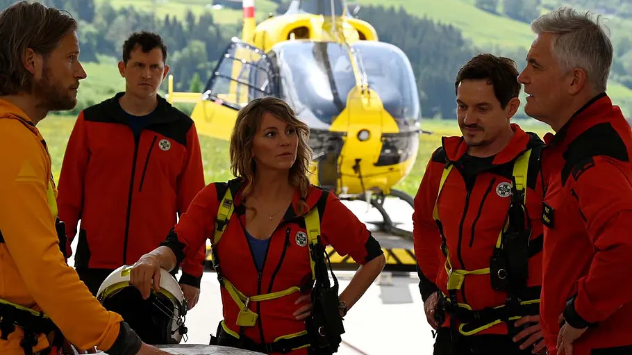 Bei „Die Bergretter“ heißt es wieder: Abschied nehmen. Markus und seine Bergretter unterhalten sich, im Hintergrund ein Helikopter.