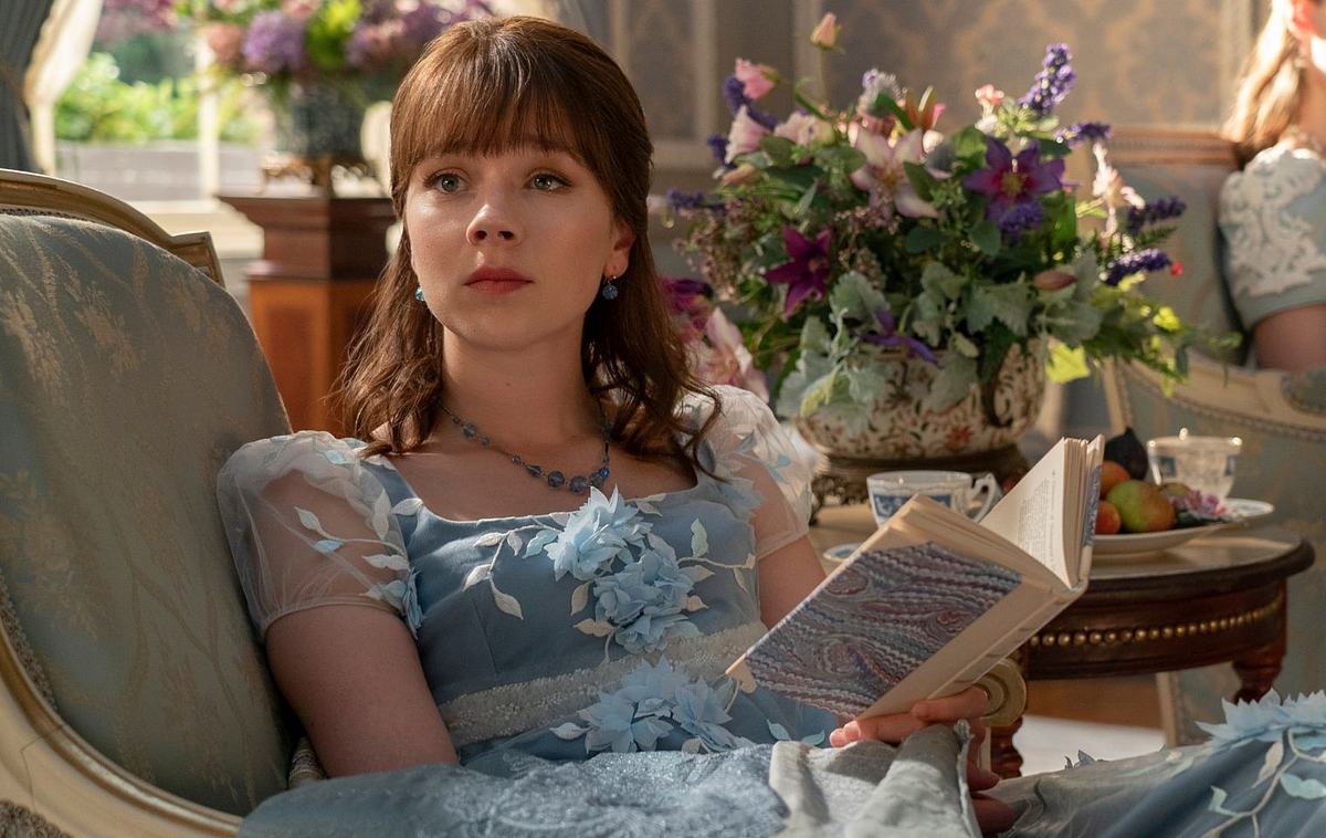 Bridgerton Eloise mit einem Buch in der Hand auf der Couch sitzend