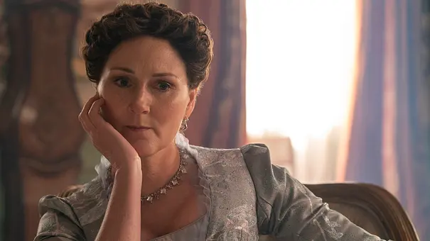 Violet Bridgerton mit hochgestecktem Haar und silbergrauem Kleid sitzt auf einem Stuhl und stützt ihre Wange auf die Hand. - Foto: LIAM DANIEL/NETFLIX