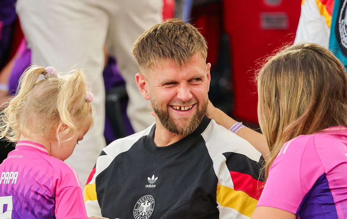 Niclas Füllkrug lachend in der Mitte, links seine Tochter Emilia, rechts seine Ehefrau Lisa, alle tragen Deutschland Trikots