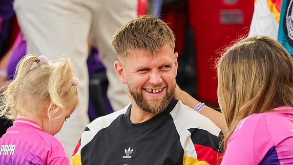 Niclas Füllkrug lachend in der Mitte, links seine Tochter Emilia, rechts seine Ehefrau Lisa, alle tragen Deutschland Trikots - Foto: dpa