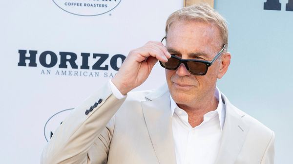 Kevin Costner im beigen Anzug schielt über seine Sonnenbrille hinweg - Foto: IMAGO / Newscom / AdMedia
