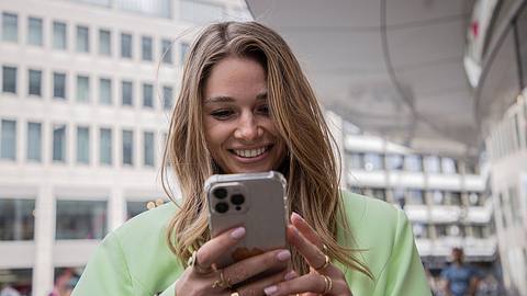 Lola Weippert trägt einen grünen Anzug und schaut lächelnd auf ihr Handy - Foto: IMAGO / Oliver Langel