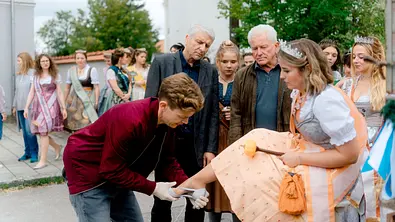 Batic und Leitmayr schauen zu wie Kollege Kalli einer Produktkönigin einen Schuh anzieht.  - Foto: BR/Odeon Fiction GmbH/Luis Zeno Kuhn