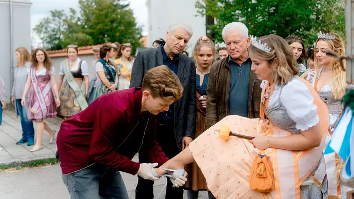 Batic und Leitmayr schauen zu wie Kollege Kalli einer Produktkönigin einen Schuh anzieht.  - Foto: BR/Odeon Fiction GmbH/Luis Zeno Kuhn
