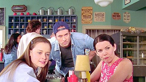 Rory, Luke und Lorelai sitzen im Café und schauen alle gebannt auf etwas - Foto: VOX/VP