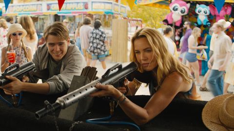 Connie Nielsen hält auf einem Jahrmarkt ein Gewehr in der Hand und spielt die Rolle der Becca in ‚Nobody 2‘. Neben ihr steht ihr Sohn, gespielt von Gage Munroe, ebenfalls mit einem Spielgewehr in der Hand. - Foto: Universal Presse