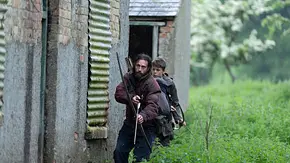 Man sieht Aaron Taylor-Johnson (vorne) als Jamie und Alfie Williams als Spike. Die beiden ziehen in Funktionskleidung und bewaffnet mit Pfeil und Bogen durch Gras an einer Hauswand vorbei. - Foto: IMAGO / Landmark Media Man sieht Aaron Taylor-Johnson (vorne) als Jamie und Alfie Williams als Spike. Die beiden ziehen in Funktionskleidung und bewaffnet mit Pfeil und Bogen durch Gras an einer Hauswand vorbei. - Foto: IMAGO / Landmark Media