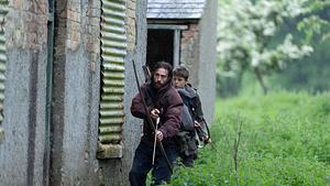 Man sieht Aaron Taylor-Johnson (vorne) als Jamie und Alfie Williams als Spike. Die beiden ziehen in Funktionskleidung und bewaffnet mit Pfeil und Bogen durch Gras an einer Hauswand vorbei. - Foto:  IMAGO / Landmark Media