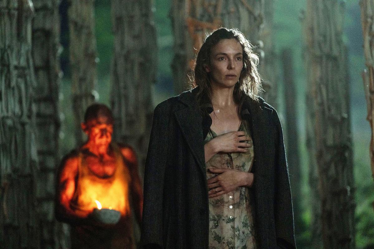 28 Years Later Jodie Comer und Ralph Fiennes sind umgeben von Säulen, die aus Knochen bestehen. Jodie Comer trägt eine schwarze Jacke, sowie ein dreckiges Kleid mit Muster. Während Ralph Fiennes in einem weißen Unterhemd von Licht erhellt wird.