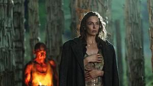 Jodie Comer und Ralph Fiennes sind umgeben von Säulen, die aus Knochen bestehen. Jodie Comer trägt eine schwarze Jacke, sowie ein dreckiges Kleid mit Muster. Während Ralph Fiennes in einem weißen Unterhemd von Licht erhellt wird. - Foto: IMAGO / Landmark Media