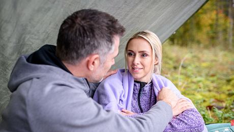 Larissa und Yannik sitzen draußen unter einer Zeltplanne. Er berührt sie an ihrer Schulter. Sie schaut ihn verliebt an. - Foto: ARD/WDR/Christof Arnold