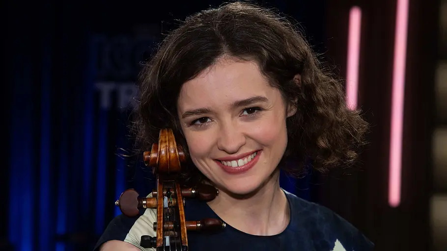Anastasia Kobekina Cellistin Anastasia Kobekina im TV-Studio: Die Musikerin lächelt in die Kamera und hält ihr Cello, im Hintergrund sind Studiolichter zu sehen