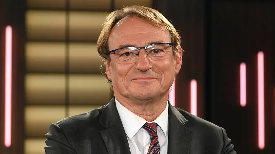 Andreas Englisch Andreas Englisch im TV-Studio: Er Journalist trägt Anzug, Krawatte und Brille und blickt mit verschränkten Armen in die Kamera