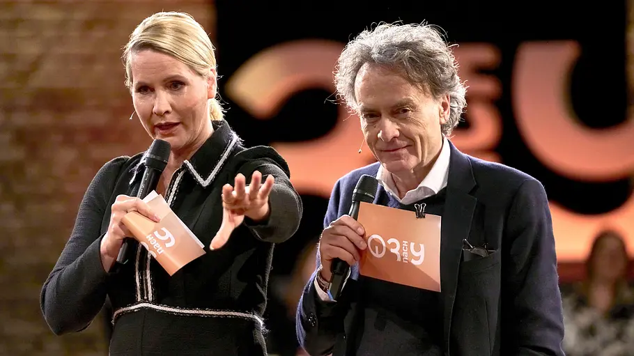 Judith Rakers und Giovanni di Lorenzo Judith Rakers und Giovanni di Lorenzo moderieren eine Talkrunde, beide halten Mikrofone und Moderationskarten in der Hand und sprechen auf einer Bühne vor Publikum