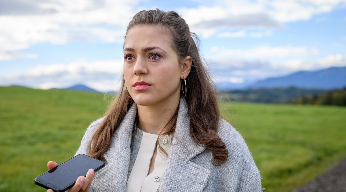 Maxi bei Sturm der Liebe Maxi hält bei Sturm der Liebe ihr Smartphone in der Hand und starrt auf einem leeren Feldweg ins Weite.