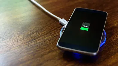 Ein Handy lädt auf einem Nachttisch auf einem Wireless Charger - Foto: iStock/yevtony