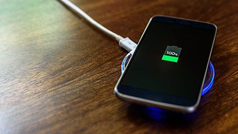 Ein Handy lädt auf einem Nachttisch auf einem Wireless Charger - Foto: iStock/yevtony