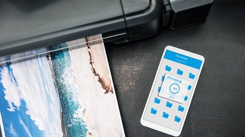 Ein an einen drahtlosen Drucker angeschlossenes Smartphone liegt auf dem Schreibtisch - Foto: iStock/baloon111