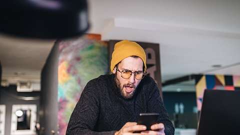 Überraschter junger Mann entdeckt Amazon Deals auf seinem Smartphone - Foto: iStock/FluxFactory