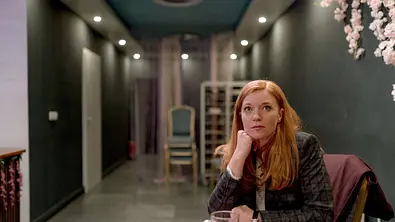 Marleen Lohse sitzt im karierten Blazer an einem Tisch mit Teeglas und stützt ihr Kinn auf die Hand. - Foto: NDR/ARD/Frizzi Kurkhaus