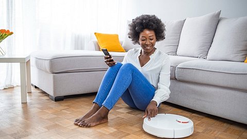 Frau sitzt neben Saug-Wisch-Roboter - Foto: iStock/dragana991