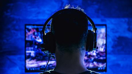 Hinterkopf eines Mannes, der ein Headset trägt und im dunklen Raum am Fernseher spielt. - Foto: kerkez/iStock