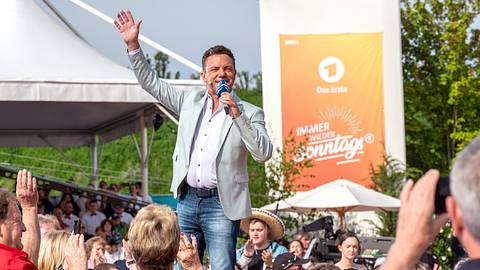 Stefan Mross steht mit Mikrofon vor dem Publikum und winkt während der ARD-Sendung „Immer wieder sonntags“ im Europa-Park Rust. - Foto: Media Press