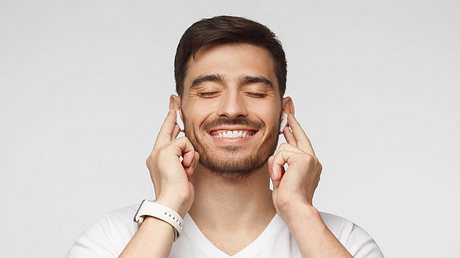 Ein Mann nutzt kabellose In-Ear-Kopfhörer. - Foto: iStock / Damir Khabirov