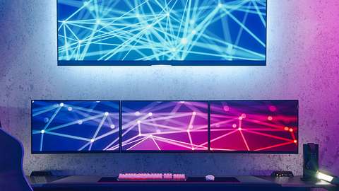 Gaming-Schreibtisch mit drei kleinen Monitoren, die nebeneinander stehen, und einem großen vierten Bildschirm, der darüber hängt. - Foto: iStock/imaginima