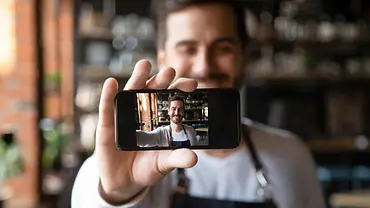 Mann hält kleines Smartphone für Selfie lächelnd vor sich - Foto: iStock/fizkes
