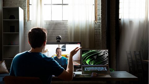 Razer Kiyo Pro Webcam auf einem Bildschirm montiert. Davor sitzt ein Mann und spricht mit einer Person auf dem Bildschirm per Videochat. - Foto: Razer/PR