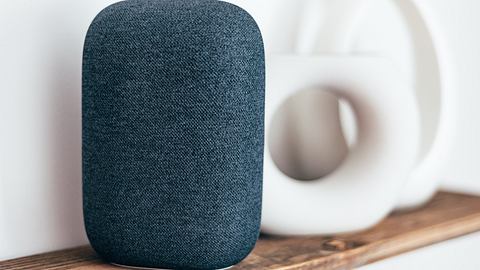 Ein intelligenter Lautsprecher in Grau auf einem Holzregal, daneben dekorative Vasen - Foto: iStock/Manuta