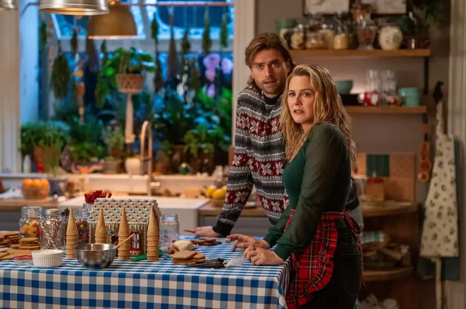 a-merry-little-ex-mas-netflix-2025.webp Ausschnitt aus A Merry Little Ex-Mas mit Pierson Fodé als Chet und Alicia Silverstone als Kate. Sie stehen in der Küche und wollen ein Lebkuchen Haus backen.