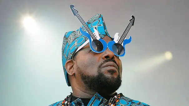 Afrika Bambaataa steht auf einer Bühne und trägt eine blaue Sonnenbrille bestehend aus zwei Bässe.  - Foto:  IMAGO / Depositphotos