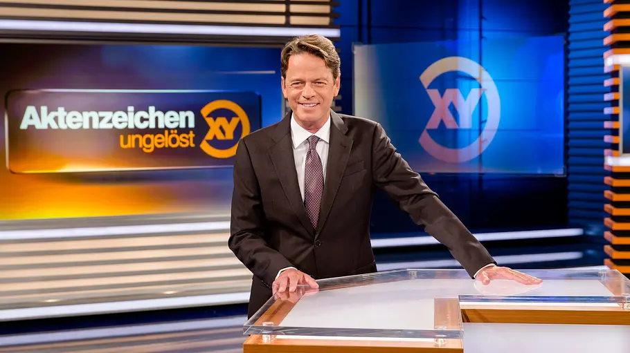 Aktenzeichen XY Rudi Cerne steht lächelnd im Studio von „Aktenzeichen XY“.