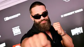 Aleks Petrovic trägt Sonnenbrille und Vollbart und hält die Fäuste in Boxpose vor einer dunklen Wand mit Logos. - Foto: IMAGO / Panama Pictures Aleks Petrovic trägt Sonnenbrille und Vollbart und hält die Fäuste in Boxpose vor einer dunklen Wand mit Logos. - Foto: IMAGO / Panama Pictures