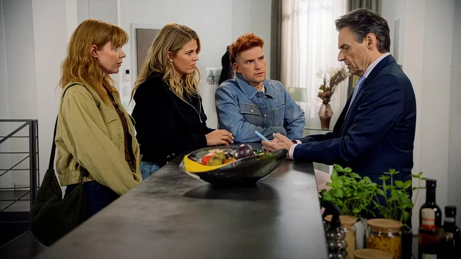 Alicia Video GZSZ Toni, Alicia und Mo stehen an einer Küchentheke und schauen ernst zu Gerner, der im Anzug ein Smartphone hält.