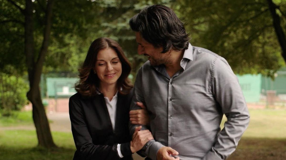 Gabriella und Maximilian bei AWZ Gabriella hängt sich in Maximilians Arm bei Alles was zählt. Er schaut sie strahlend an, sie lächelt und schaut auf den Boden.