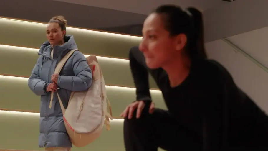 Charlie macht Dehnübungen auf dem Eis, Joana beobachtet sie dabei.