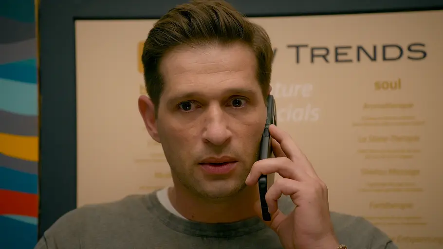 ALLES WAS ZÄHLT-Vorschau FOLGE 5067 Dienstag 3. November Deniz hält ein schwarzes Smartphone ans Ohr und blickt nach vorn. Er trägt ein graues Shirt, hinter ihm hängt ein Plakat.