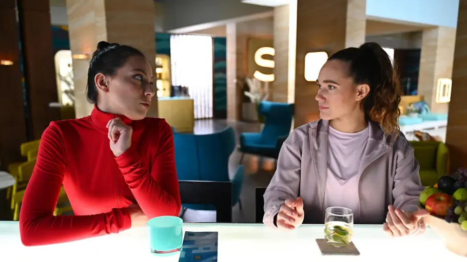 Joana und Charlie sitzen nebeneinander an der Bar. Beide sehen angespannt aus.