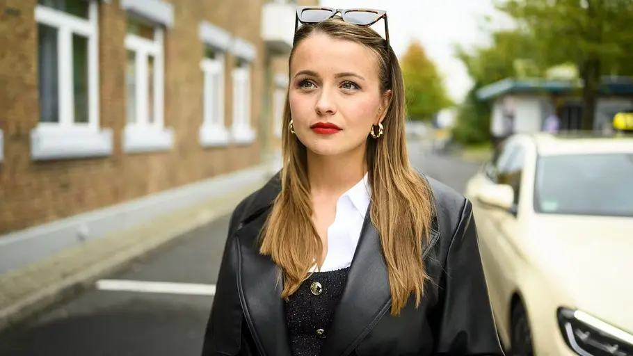 Lucie steht vor einem Taxi und schaut verträumt nach vorne.