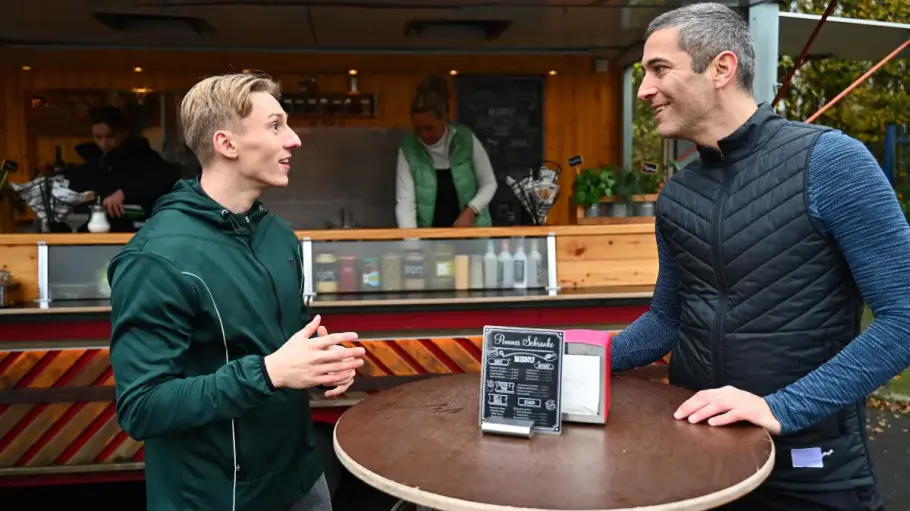 Dragan und Lennox vor einem Currywurstwagen. Beide lächeln und führen ein Gespräch