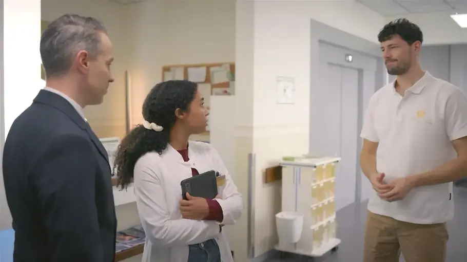 Imani hält ihre Notizen nah an ihre Brust. Sie steht zwischen Mika und Kilian und schaut völlig überrascht zu Jans Zwilling.