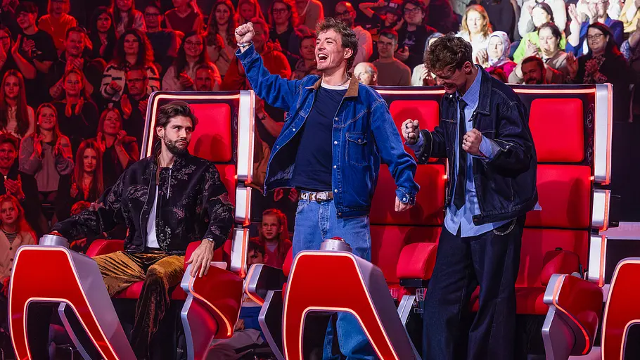 Neue Moderatorin bei „The Voice Kids“: Diese Wahl kommt überraschend Zwei Männer jubeln stehend vor roten Sesseln, ein dritter sitzt daneben. Im Hintergrund applaudiert das Publikum.