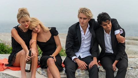 Vier Personen aus „We were Liars“ sitzen in schwarzer Kleidung mit Alkohol am Strand. - Foto: Courtesy of Prime Video / Amazon MGM Studios